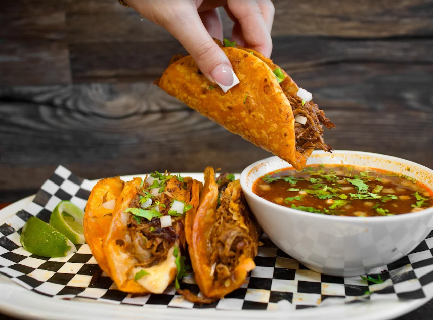 Birria tacos being dipped into consommé